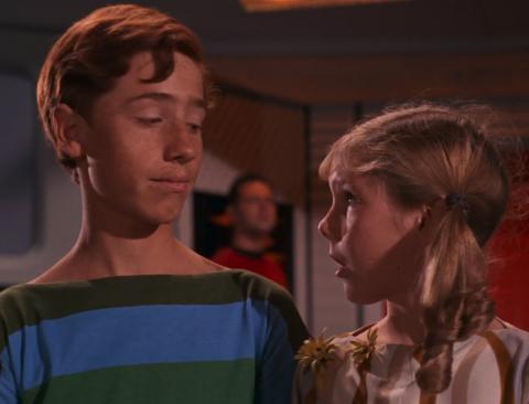 A boy with many freckles talks to a shorter girl with blond hair